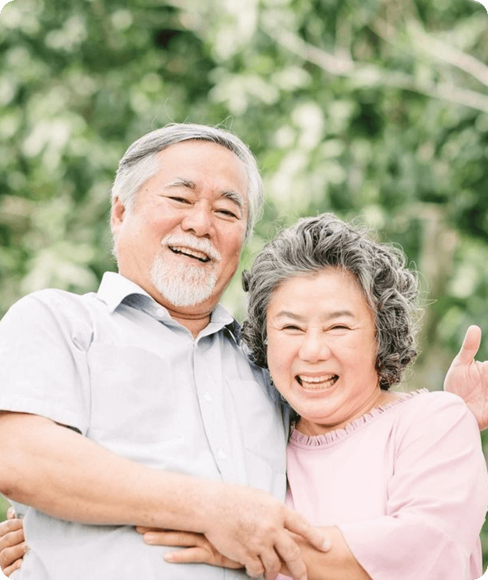 An older couple posing for a picture in front of trees.